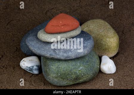 Rocce e ciottoli assortiti accatastati su una spiaggia di sabbia bagnata Foto Stock