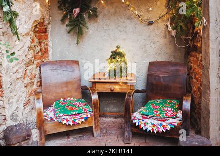 Spazio famiglia di Natale in giardino o portico anteriore. Decorazioni rustiche all'aperto in stile boho. Vecchio tavolo rustico in legno e poltrone. Messa a fuoco selettiva, niente neve Foto Stock