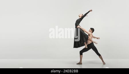 Giovane uomo e donna, ballerini ballerini che si esibiscono isolati su sfondo grigio studio. Supporto e volo. Volantino Foto Stock