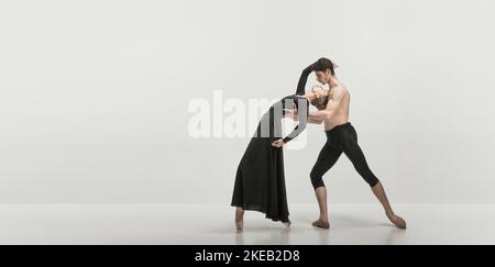 Giovane uomo e donna, ballerini ballerini che si esibiscono isolati su sfondo grigio studio. Relazione appassionata Foto Stock