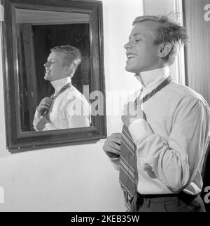 Vestirsi con la 1950s. Un giovane uomo davanti allo specchio gli node la cravatta. Ci sono varianti di legatura della cravatta tra cui Ascot, prua, bolo, cravatta con cerniera, cravat e maglia. Al momento in cui la foto è stata presa la moda e lo sguardo delle cravatte erano più sottili e sottili che i decenni precedenti. Ci sono quattro nodi principali utilizzati per il nodo cravatta: Quattro in mano nodo, Pratt nodo, mezzo Windsor nodo e Windsor nodo. Svezia 1959. Rif. Conard 4019 Foto Stock