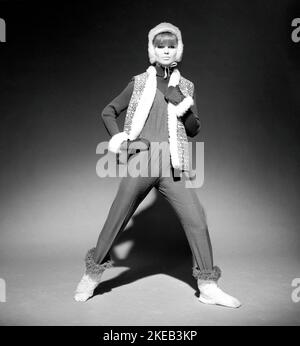 Negli anni '1960s. Un modello di moda, in tipico abbigliamento invernale 1960s in uno studio. Ha una tuta sottile sulla parte superiore sopra un maglione lavorato a maglia a maniche lunghe insieme ad un gilet, guanti e cappuccio. Svezia 1966 Foto Stock