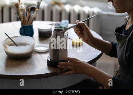 Donna professionista proprietario piccola impresa ceramica tiene pennello in mani e processi in miniatura vaso Foto Stock