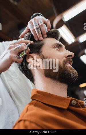 vista ad angolo basso del taglio capelli stilista di uomo sorridente bearded, immagine di scorta Foto Stock