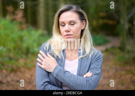 Bella donna bionda di mezza età in piedi in una foresta con le braccia incrociate e gli occhi chiusi Foto Stock