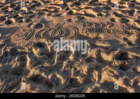 Iscrizione 'Happy Halloween' e faccia disegnata e zucca in spiaggia di sabbia nelle giornate di sole. Foto Stock