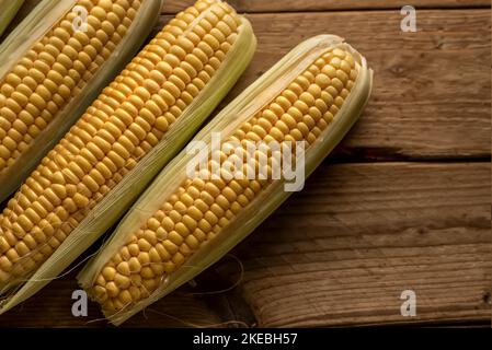 Tre spighe di mais (Zea mays) su sfondo rustico in legno. Vista dall'alto. Foto Stock
