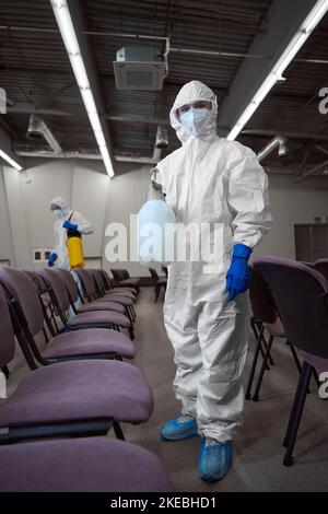 Pulitore indossare indumenti protettivi durante la disinfezione dei mobili Foto Stock