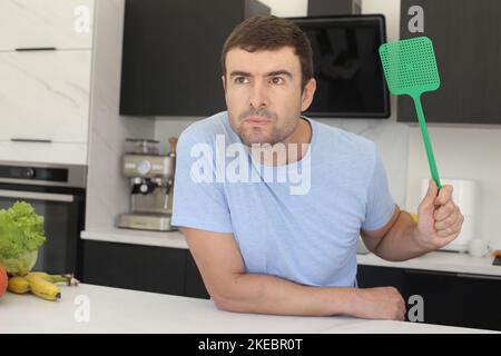 Uomo che cerca di prendere una mosca in cucina Foto Stock