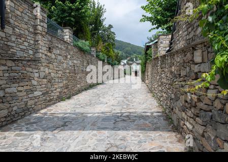 Strada asfaltata e pareti in pietra all'ingresso del piccolo villaggio di montagna di Nymfaio nel nord della Grecia. Foto Stock