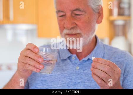 primo piano e ritratto di un uomo maturo o senior medicamento e cuscini con un bicchiere d'acqua - malato e mal pensionato Foto Stock