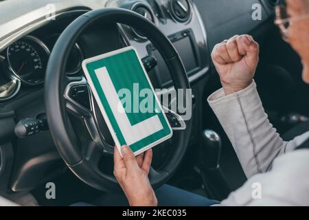 Una donna anziana ottiene il pass per guidare un'auto in età matura. Senior guardando al permesso L nel sedile di guida per celebrare il successo Foto Stock