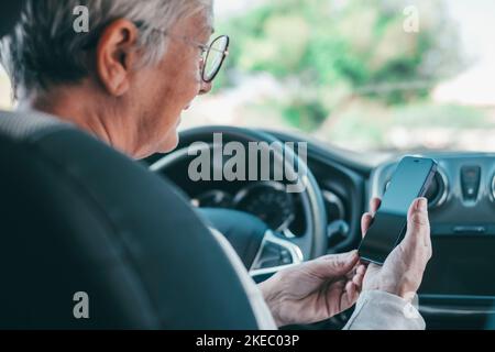 Ritratto di una donna anziana che utilizza il telefono in auto durante la guida su strada rischio di incidenti. Primo piano con lo smartphone per navigare in chat e inviare SMS online. Foto Stock