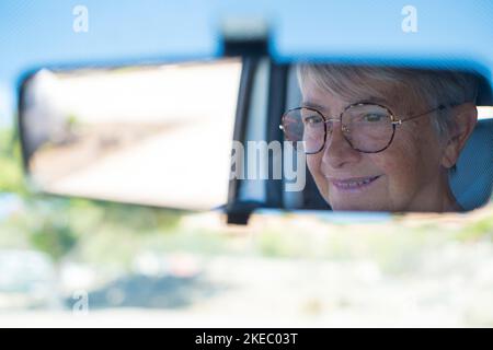 Primo piano di una donna anziana che guarda la strada durante la guida. Specchio posteriore della vettura. Cliente soddisfatto che utilizza una nuova vettura. Concetto di cliente soddisfatto Foto Stock