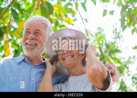 Coppie anziane che si abbracciano nel parco primaverile all'aperto divertendosi e godendosi insieme guardando gli alberi. Due persone anziane e mature che si amano si prendono cura l'una dell'altra. Foto Stock