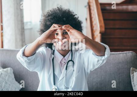 Donna medico che fa il gesto a forma di cuore con le mani. Sorridente dottoressa nera che fa un simbolo d'amore usando le sue mani. Operatore sanitario che esprime amore e sostegno ai pazienti Foto Stock