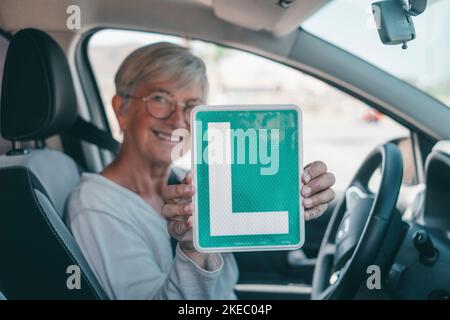 Una donna anziana ottiene il pass per guidare un'auto in età matura. Senior guardando al permesso L nel sedile di guida per celebrare il successo Foto Stock