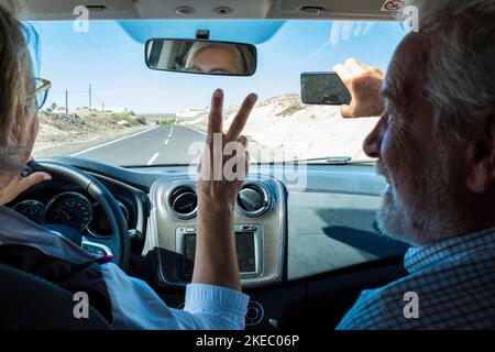 coppia di anziani e pensionati in auto guida e. prendere un selfie insieme sorridendo e guardando la fotocamera Foto Stock