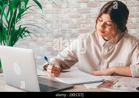 Donna sorridente scrivere appunti guardare webinar studio lavoro su laptop, giovane studente imparare corso di computer ascoltare lezione formazione interprete online insegnante di traduzione classe Foto Stock