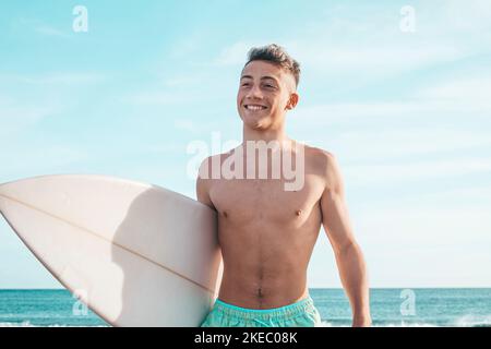 ritratto di bel giovane uomo che cammina sulla spiaggia con la sua tavola da surf pronta a cavalcare le onde e a fare surf il suo tempo di vacanza Foto Stock