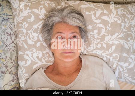 Donna anziana insomaniaca sdraiata a letto guardando in alto e cercando di dormire. Vista dall'alto dell'infelice sensazione di anziana disturbata da insonnia. Donna depressa che ha problemi sdraiata in camera da letto a casa Foto Stock