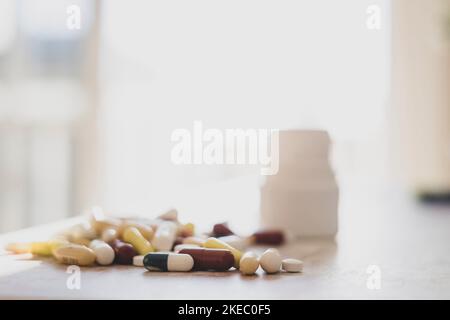 Primo piano di compresse multicolori assortite, pillole, capsule con flacone sul tavolo a casa, mucchio di medicine sul tavolo. Diversi farmaci colorati e pillole sul tavolo bianco da laboratorio Foto Stock