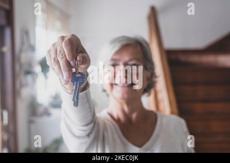 Felice anziano anziano donna anziano cliente proprietario tenere la chiave a casa nuova appartamento dare alla macchina fotografica, anziano donna pensionato proprietario di bene immobile fare vendita acquisto concetto di affare di proprietà, primo piano in su vista Foto Stock