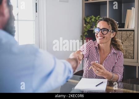 Donna d'affari felice che scuote la mano con il cliente maschio dopo l'affare o la firma del contratto all'ufficio. Donna di vendita sorridente che fa una stretta di mano con il cliente o candidato di lavoro alla riunione di affari di occupazione Foto Stock