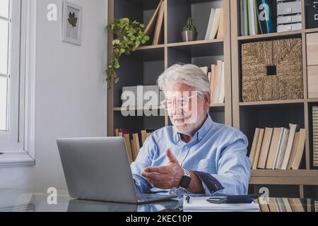 Buon vecchio uomo d'affari caucasico sorridente lavorando online guardando il podcast del webinar sul laptop e sull'apprendimento corso di formazione chiamata conferenza prendere appunti seduti alla scrivania, concetto di elearning Foto Stock