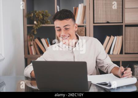 Felice giovane uomo d'affari caucasico sorridente lavorando online guardando il podcast del webinar su laptop e imparare corso di formazione conference call prendere appunti seduti alla scrivania, concetto di elearning Foto Stock