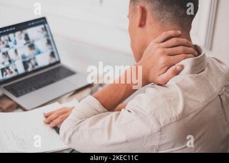 Primo piano vista posteriore stressato giovane uomo che tocca il collo inferiore sensazione di disagio, che soffre di dolore improvviso a causa di uno stile di vita sedentario o lungo lavoro sul computer in una postura errata in ufficio a casa. Foto Stock