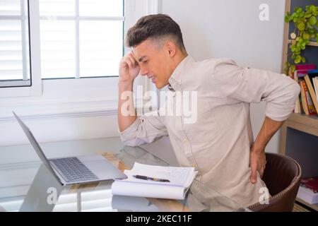 Primo piano vista posteriore stressato giovane uomo che tocca la parte inferiore della schiena sensazione di disagio, che soffre di dolore improvviso a causa di uno stile di vita sedentario o lungo lavoro sul computer in una postura errata in ufficio a casa. Foto Stock