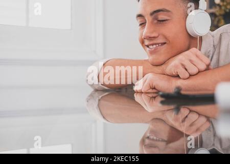 Giovane adolescente tranquillo e spensierato a casa, indossa moderne cuffie wireless, ascolta la musica classica preferita online, sentiti tranquillo e consapevole da solo nel salotto di casa. Foto Stock