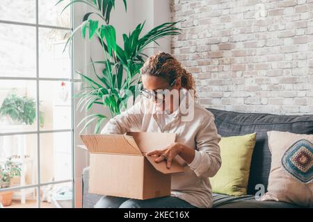 Donna overjoyed seduta sul divano tenere in giro piccolo cartone scatola aperta pacco cliente ritiene soddisfatto acquistato merci in internet, felice destinatario ricevuto pacchetto da amico, servizio di consegna rapida concetto Foto Stock