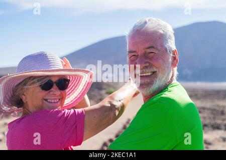 coppia di anziani in una vacanza insieme divertendosi - due persone mature che guardano la macchina fotografica sorridendo e ridendo - donna che inndicava qualcosa con il braccio Foto Stock