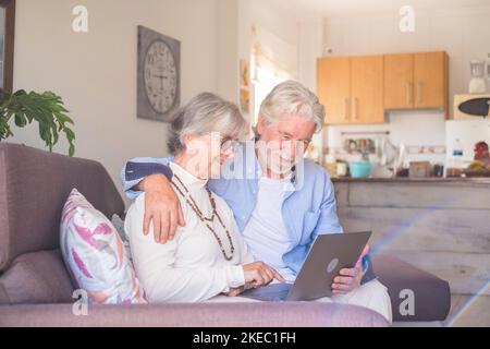 Coppia di due persone anziane e mature a casa utilizzando un tablet insieme in un divano. Notebook per uso senior che si diverte e si diverte a guardarlo. Concetto di tempo libero e libero Foto Stock