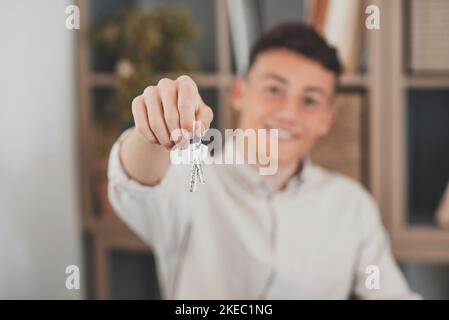 Focus su mazzo di chiavi da casa appartamento in mano di sorridente adolescente. Ritratto sfocato di uomo fiducioso realtor professionale che offre nuova unità immobiliare abitazione al potenziale acquirente. Primo piano Foto Stock