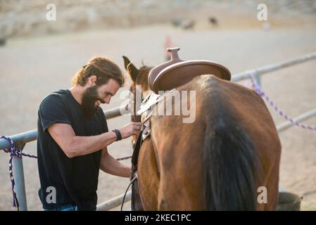 un uomo da solo in un ranch che si prende cura di a. horse - sorridendo e divertendosi a risolvere - horse pronto a correre e pronto ad andare via con lui cowboy Foto Stock