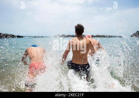 gruppo di tre adolescenti e giovani che si godono le vacanze estive in spiaggia nuotare e correre al mare o. oceano sorridente e ridente - gente felice con i capelli colorati divertirsi Foto Stock