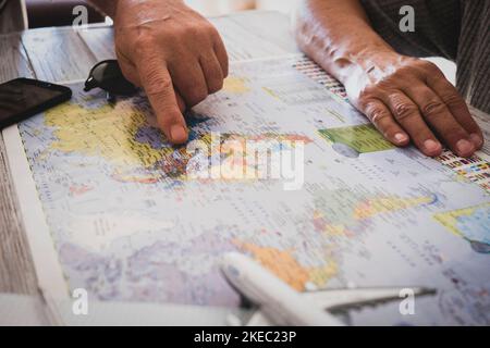 Persone anziane e irriconoscibili che pianificano un nuovo viaggio - senza limiti di età per lo stile di vita del vagabondo - Coppia caucasica e mappa del mondo con il giocattolo dell'aeroplano sul tavolo - viaggiatore e vacanza Foto Stock