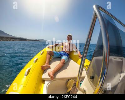 primo piano e ritratto di giovane e felice uomo bello goditi l'estate sdraiata su una piccola barca o un gommone in mezzo al mare - maschio con abs sorridendo guardando la macchina fotografica nelle sue vacanze Foto Stock