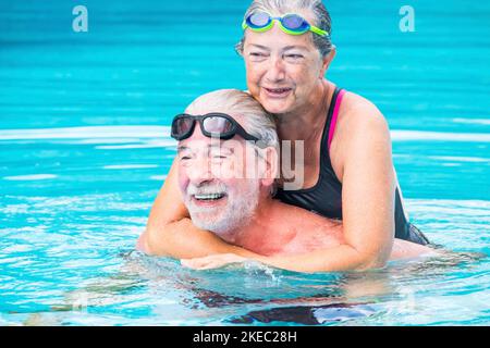 due pensionati o anziani maturi che si godono l'estate e le vacanze in piscina insieme divertendosi sorridendo e ridendo - coppia di anziani carino in amore - stile di vita felice e concetto sano Foto Stock