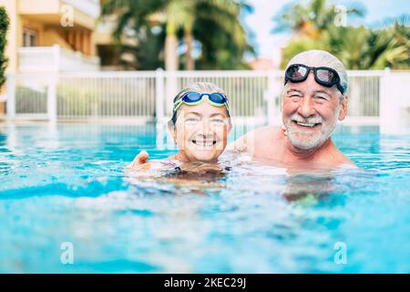 coppia degli anziani e dei pensionati carini nell'acqua di la piscina si diverte e si diverte insieme - due maturo persone innamorate guardando la macchina fotografica - facendo esercizio e allenarsi insieme sorridendo Foto Stock