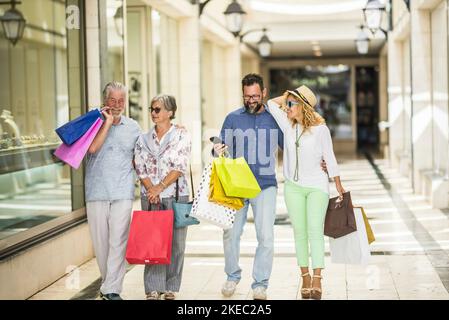 gruppo di quattro persone di adulti e anziani che fanno la spedizione insieme in un centro commerciale con un sacco di shopping borse - l'uomo che guarda il suo telefono Foto Stock