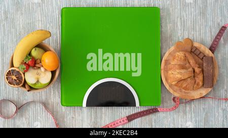 primo piano e ritratto della bilancia a pavimento con frutta e cibo sano a sinistra e cibo malsano a destra Foto Stock