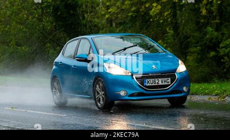 c2013 blu Peugeot 208 ar guida sotto la pioggia su una strada bagnata Foto Stock