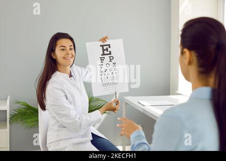 L'oftalmologo controlla la vista della donna puntando a piccole lettere sulla carta per il test visivo. Foto Stock