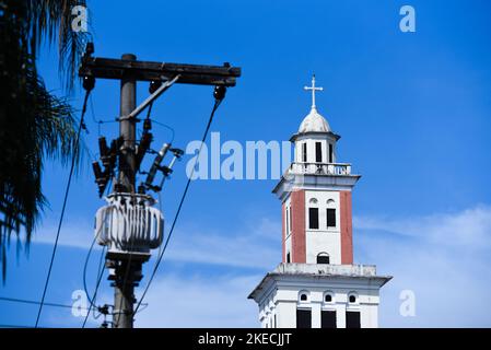 Trasformatore elettrico con cavi e Campanile di una Chiesa nel cielo blu Foto Stock