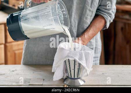 Fasi per la preparazione del latte di mandorla, donna filtra la massa dal frullatore attraverso un panno di garza Foto Stock