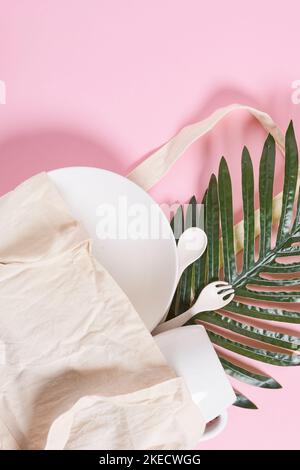 un piatto bianco e alcune foglie verdi su sfondo rosa con un sacchetto di carta vuoto nell'immagine è preso dall'alto Foto Stock